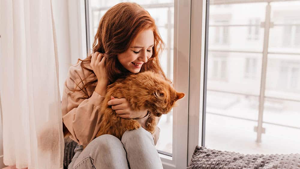 Woman with her cat sitting beside the window.