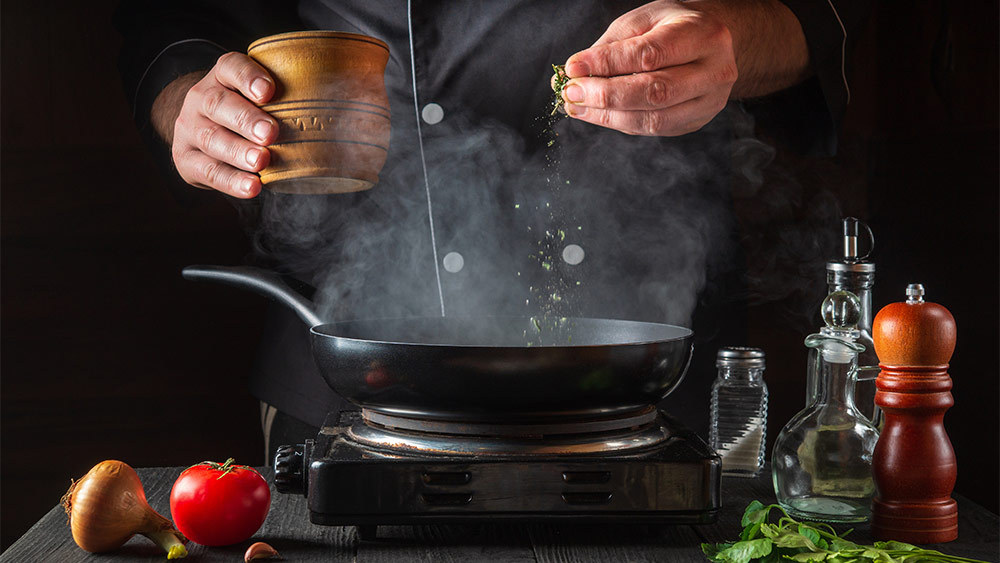 A man cooking on a stove top to help warm up a room without a heater