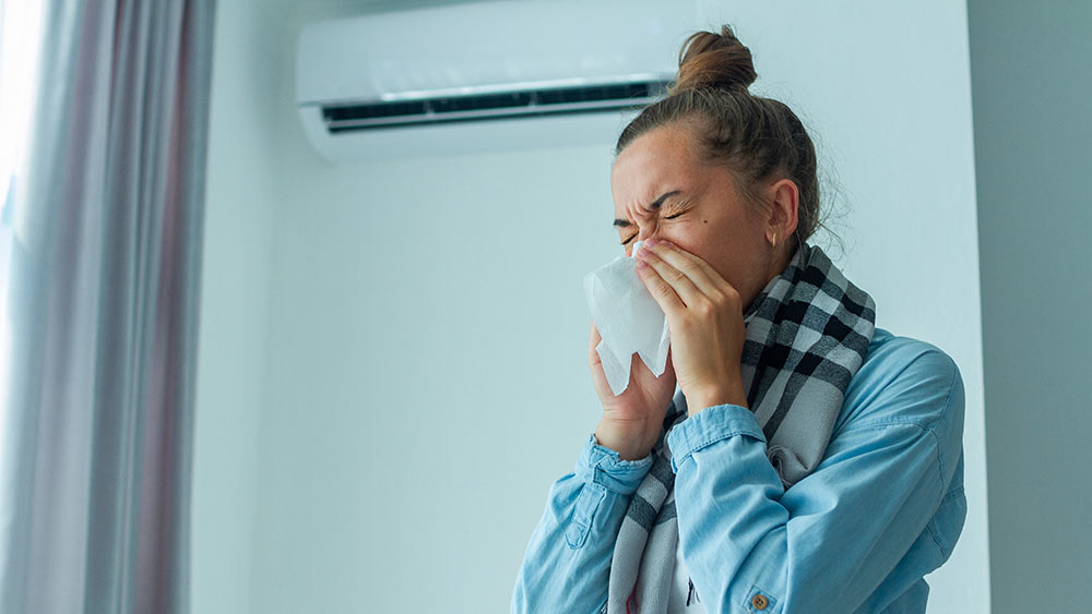 Woman sneezing as mold growth in her AC is aggravating her allergy issues