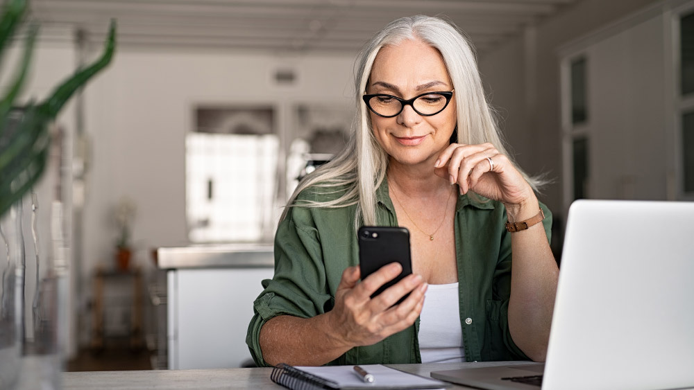 A woman using her phone to adjust AC settings. With smart thermostats, you can make changes from anywhere, which makes hem worth investing in. 