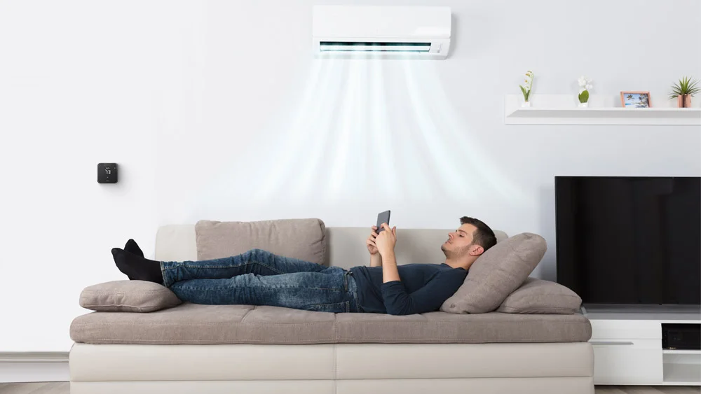 man lying on sofa using phone. Breez Max, a mini-split thermostat, is paired with mini-split to maintain ideal temperature 