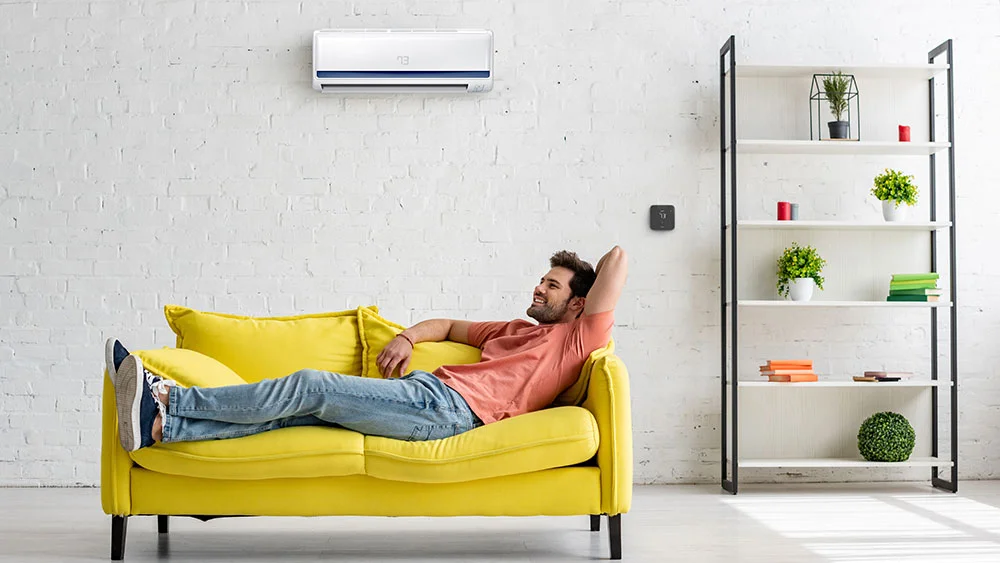 man relaxing on yellow sofa with max controlling the mini-split